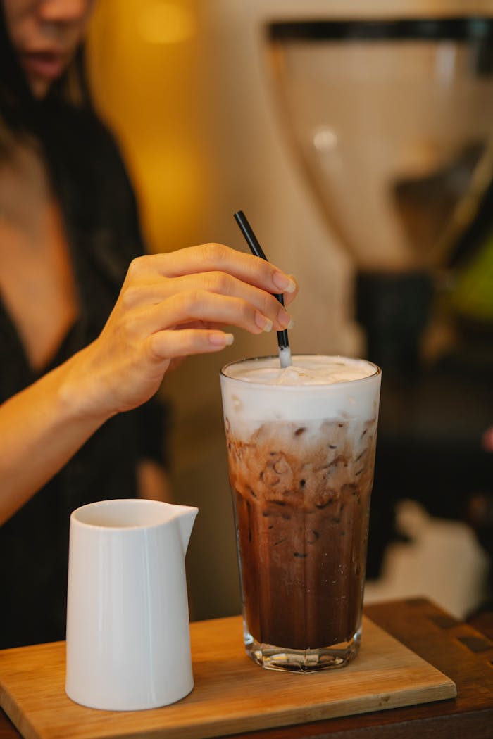 Crop woman putting straw into glass of iced coffee latte